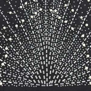 Détail de robe en maille noire ornée de perles et strass disposés en éventail radial