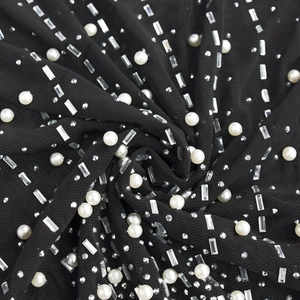 Détail du tissu en maille noire avec strass scintillants et perles blanches sur la robe
