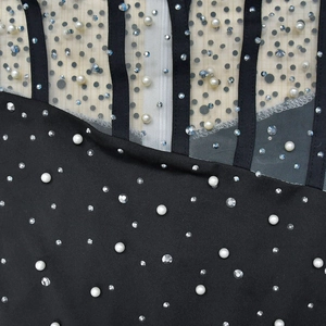 Détail de tissu noir avec mesh, perles blanches et strass étincelants sur le vêtement chic