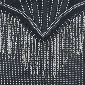Vue macro d'une robe en maille noire avec strass argentés et détails de franges en métal