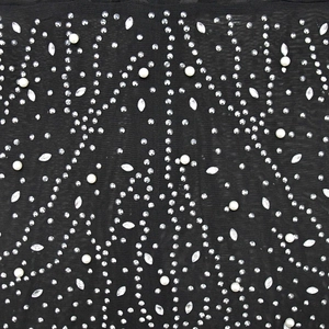 Détail macro du tissu en résille noire avec des strass argentés et des perles blanches