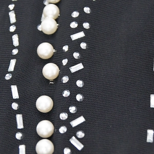 Detailed close-up of white pearls and sparkling rhinestones on black mesh fabric