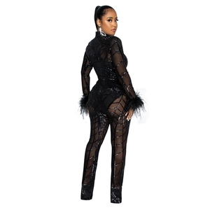 Detail of sheer mesh jumpsuit with black sequins, geometric patterns and feather cuffs