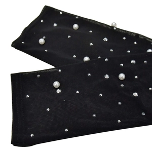 Détail de manches en maille noire ornées de perles blanches et de strass scintillants