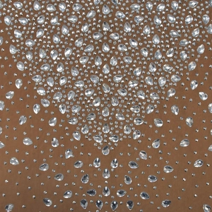 Detailed view of luxury rhinestones and teardrop crystals on tan mesh dress fabric