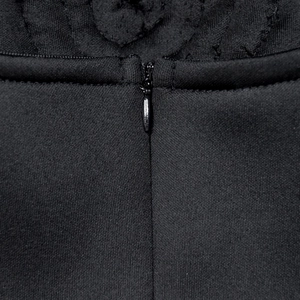 Detailed close-up of a hidden zipper on a black sleeveless dress with lace stitching
