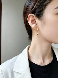 Detail of polished gold hoop earrings on a model paired with a white blazer
