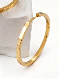 Macro shot of gold faceted geometric hoop earrings featuring modern textured metal finish
