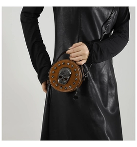 Detail of a brown leather round crossbody bag with a metallic skull and stud accents