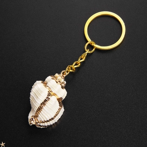 Natural shell keychain with gold beach conch pendant on elegant black texture