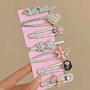 Détail de 7 barrettes en métal avec perles et strass sur une carte rose