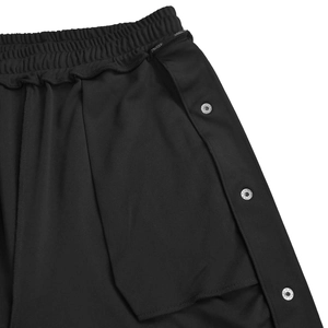 Dettaglio dei pantaloni sportivi neri con bottoni a pressione laterali e vita elastica