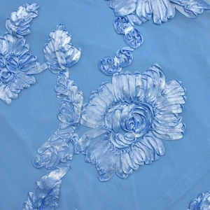 Close-up of light blue mesh fabric featuring detailed ribbon embroidery floral patterns