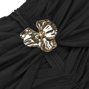 Détail du tissu plissé noir avec une grande fleur métallique dorée et une fermeture éclair