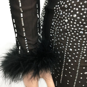 Dettaglio dell'abito in mesh con strass e polsini in piume nere e cristalli lucenti