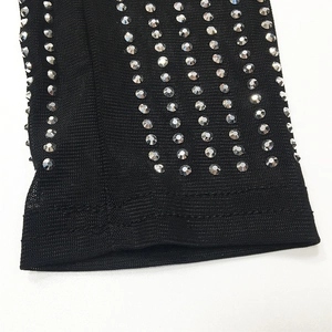 Détail du tissu en maille noire orné de rangées de strass brillants sur la manche
