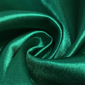 Close-up of emerald green satin fabric texture showing smooth glossy silk finish