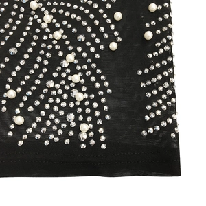Close-up of black mesh fabric with silver rhinestones and white pearls in swirl patterns