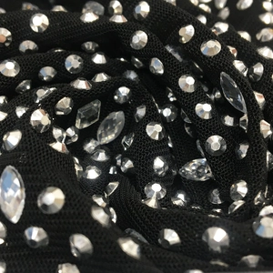 Detailed close-up of sparkling rhinestones and crystal studs on black sheer mesh fabric