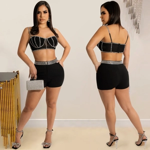 Detail of black rhinestone camisole and high-waisted shorts set with silver sequin clutch