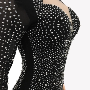 Détail de la robe en maille noire avec strass argentés et perles sur le décolleté en V