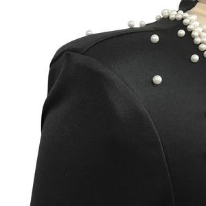 Detail of black mesh dress showing white pearl beads sewn on the neckline and shoulder