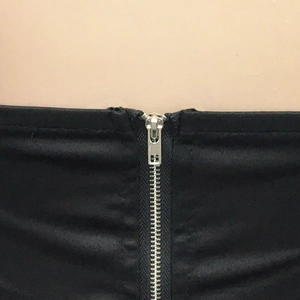 Detail of silver metal zipper on black elastic tube dress fabric showing texture