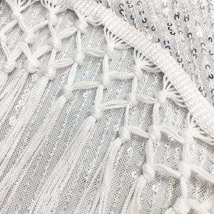 Détail du tissu en maille blanche avec paillettes argentées et franges tissées à la main