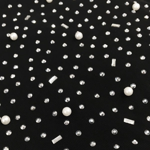 Detaillierte Makroansicht von schwarzem Netzstoff mit Strass und weißen Perlen auf dem Kleid