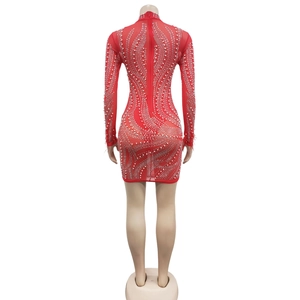 Détail d'une robe rouge en mesh avec perles blanches, strass et plumes aux poignets au dos