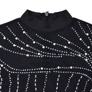 Dettaglio dell'abito in mesh nero con strass e perle bianche sul collo a lupetto