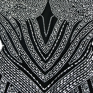 Macro detail of intricate silver rhinestones on black mesh fabric for elegant party dresses