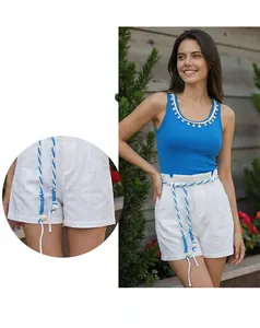 Close-up of white linen shorts with blue and white woven rope belt featuring fringe details