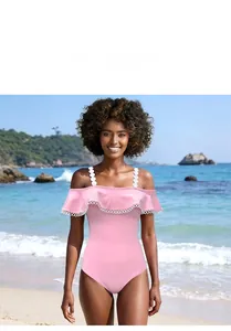 Dettaglio del costume da bagno rosa con spalle scoperte e pizzo a pois su sfondo di spiaggia