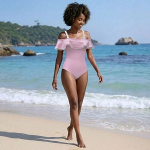 Costume intero rosa con volant a pois e spalline ad anello bianche su sfondo di una spiaggia