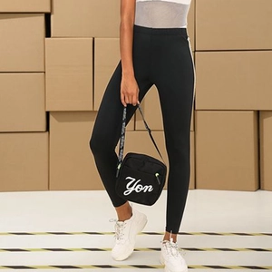 Woman in black leggings and sneakers carrying a square crossbody bag with letter print