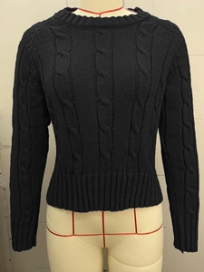 Detail of classic black cable-knit sweater showing intricate texture and ribbed hem