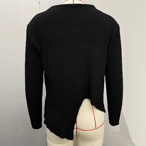 Détail du pull en maille côtelée noire présentant un ourlet asymétrique fendu au dos