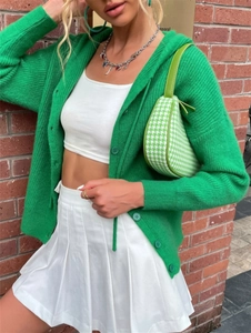 Detail shot of green knit hooded cardigan with white crop top and pleated skirt