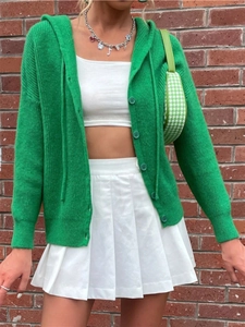 Detail of chunky green hooded cardigan with knitted buttons and white pleated skirt