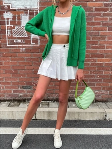 Close-up of a green hooded knit cardigan styled with a white pleated skirt and bag