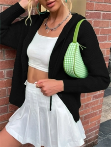 Detail of a black knit cardigan with buttons paired with a green houndstooth shoulder bag