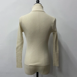 Detail of the back profile of a beige ribbed turtleneck sweater on a mannequin