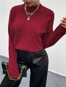 Detail eines weinroten Strickpullovers mit goldenen Halsketten und Kettenhandtasche kombiniert