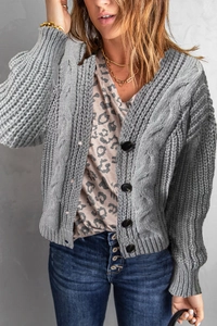 Detail of grey cable knit cardigan featuring large black buttons and textured knit pattern