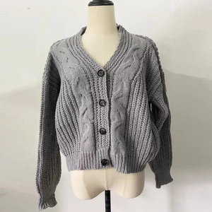 Detail of grey chunky knit cardigan featuring cable stitch pattern and V-neckline button closure