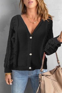 Close-up of black cable-knit cardigan featuring large decorative silver buttons and V-neck