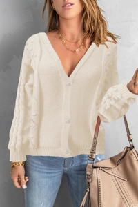 Detailed close-up of cable knit patterns and round buttons on off-white V-neck cardigan