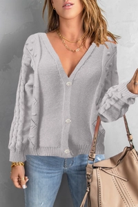 Detail of light gray knit cardigan featuring cable knit sleeves and textured pom-pom accents