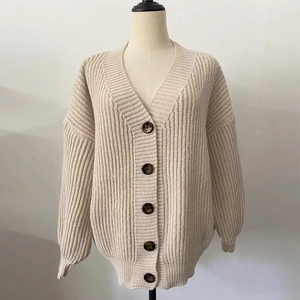 Close-up of beige chunky knit cardigan with V-neckline and dark tortoiseshell buttons